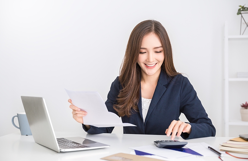 Portrait of asian business woman paying bills online with laptop in office. Beautiful girl with computer and chequebook, happy paying bills. Startup business financial calculate account concept